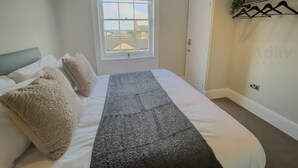 Een slaapkamer met een bed, een raam, een deur en een kapstok.