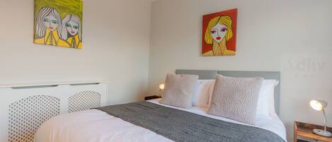 Une chambre à coucher avec un lit, une table de chevet et deux tableaux accrochés au mur.