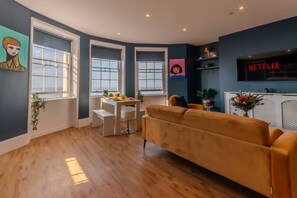 Una sala de estar moderna con un sofá, una mesa de comedor y un televisor montado en la pared.