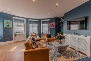 A modern living room with a sofa, armchairs, a coffee table, and a TV mounted on the wall. - Stunning Sea View Georgian Retreat by Adliv (Margate)