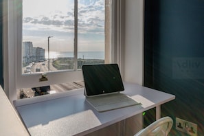 Un ordenador portátil sobre un escritorio blanco cerca de una ventana con vistas a una carretera y edificios.