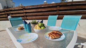 A round glass table with a white frame, surrounded by four blue chairs, set on a tiled patio with a wooden fence in the background. - Sobella Villa - 3 Bedroom Villa With 10 x 4 Pool (Paralimni)