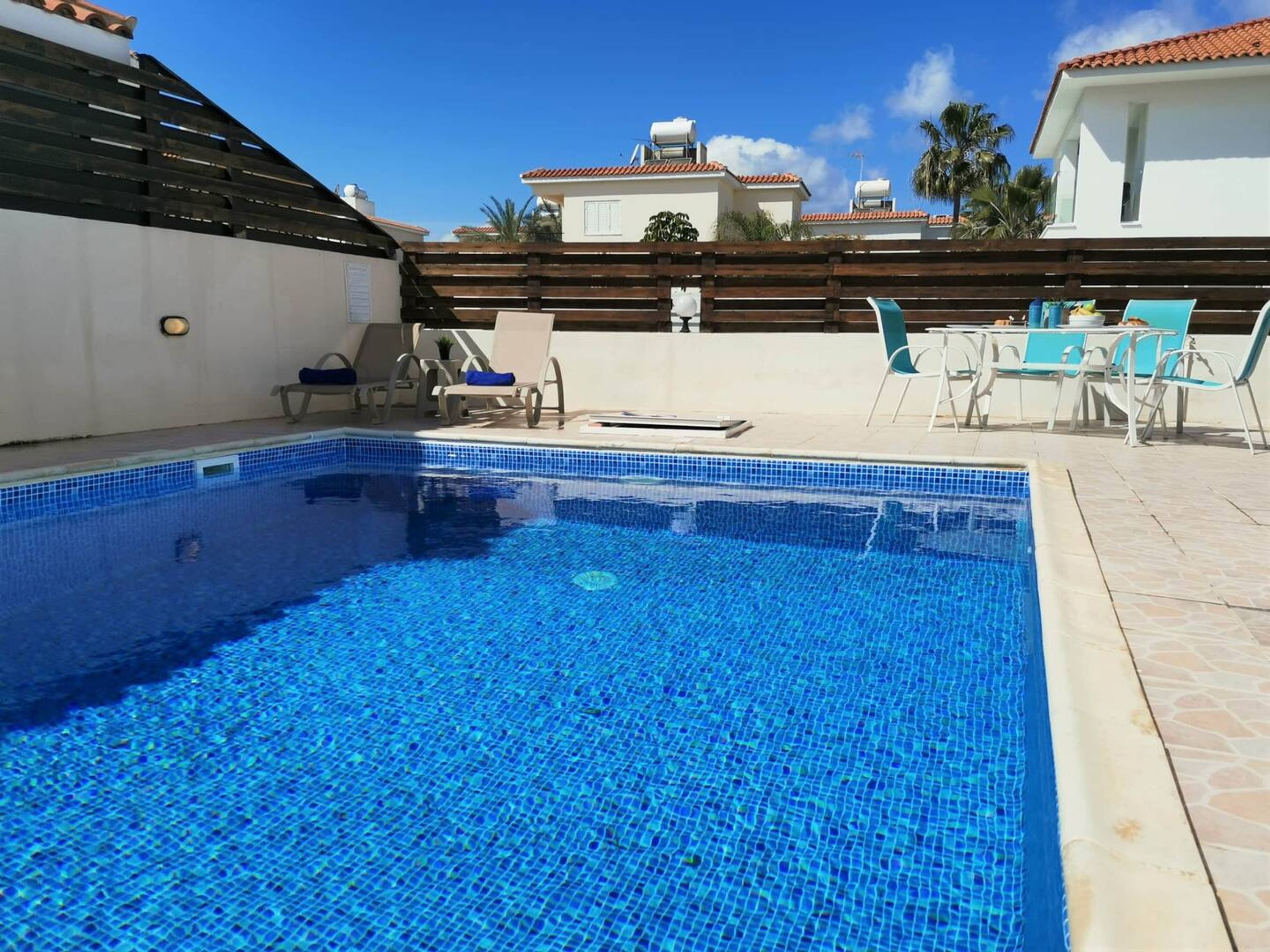 Ein rechteckiger Pool mit blauen Mosaikfliesen, umgeben von einer Holzterrasse und weißen Liegestühlen.
