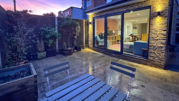 A patio with two wooden benches, a stone wall, and a glass door leading to a room with a sofa and a table.