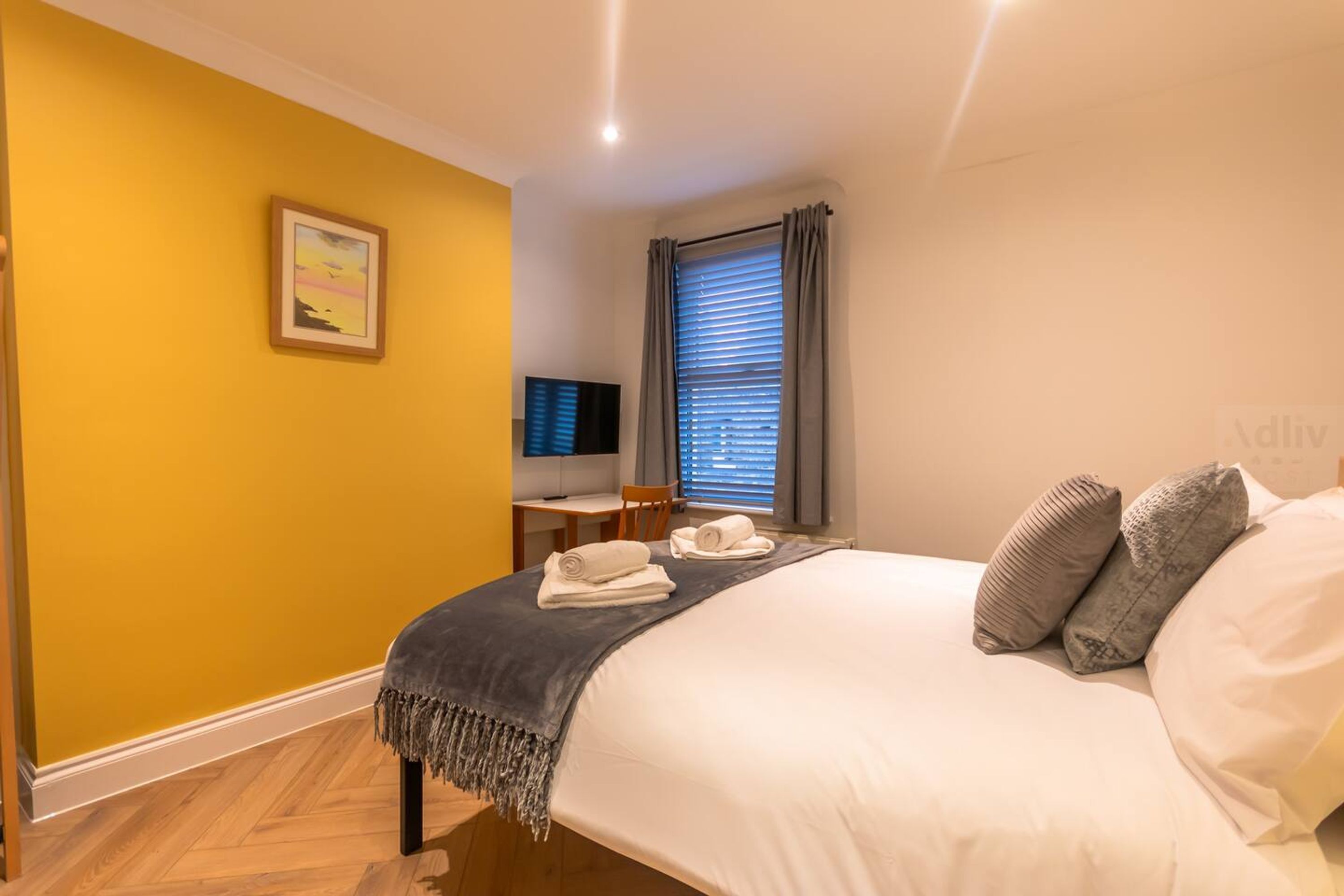 A hotel room with a bed, a desk with a chair, a television, and a window with curtains.
