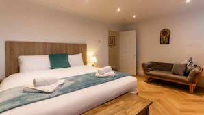 A hotel room with a large bed, a wooden headboard, a sofa, and a wooden floor.