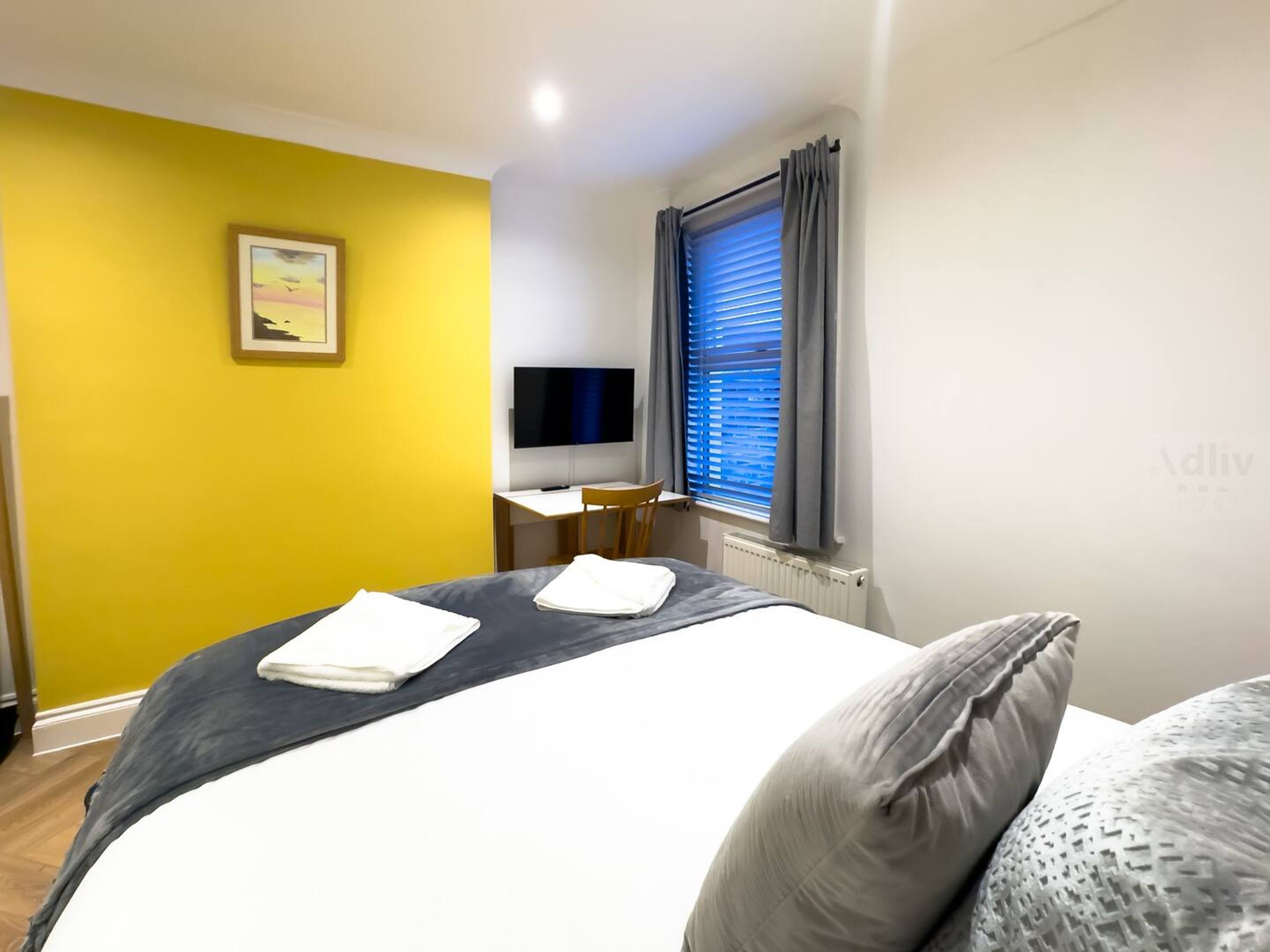 A hotel room with a bed, a desk, a chair, a TV, and a window with curtains.