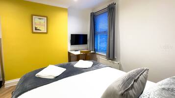 A hotel room with a bed, a desk, a chair, a TV, and a window with curtains.