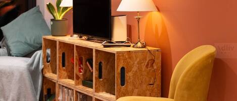 A cozy room with a wooden TV stand, a yellow chair, a potted plant, and a lamp.