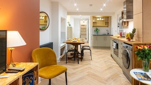 A modern kitchen with a dining area, a washing machine, and a TV.