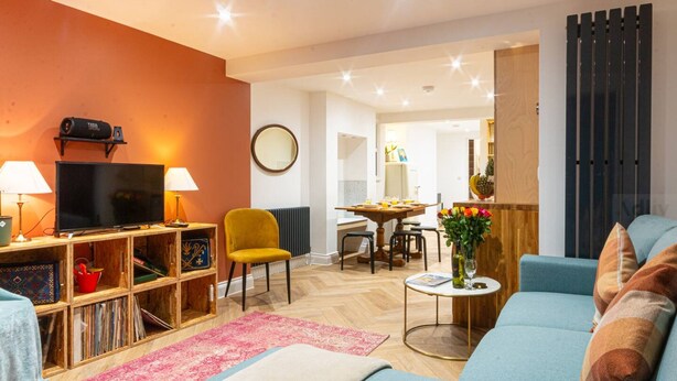 A modern living room with a sofa, a television, a bookshelf, and a dining area in the background. - Modern Margate Maisonette Close to Beach by Adliv (Margate)