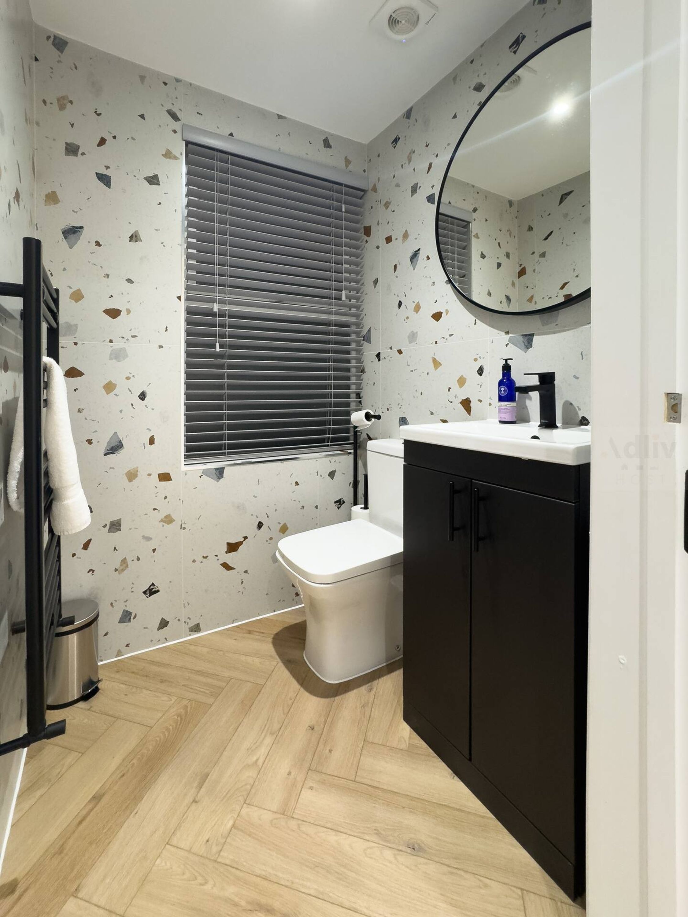 A bathroom with a white toilet, a black cabinet, a mirror, and a window with blinds.