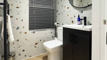 A bathroom with a white toilet, a black cabinet, a mirror, and a window with blinds.