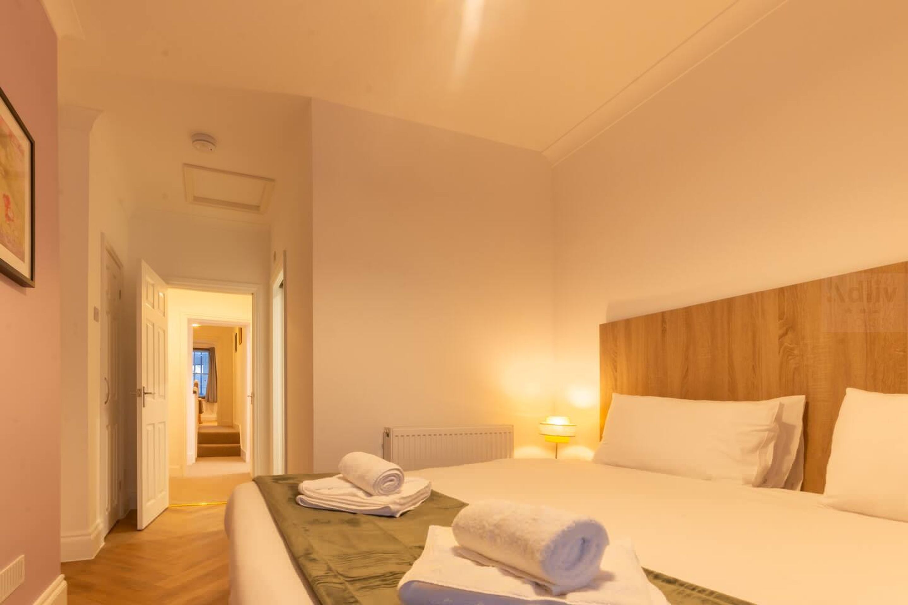 Hotelkamer met een bed, nachtkastje, lamp en uitzicht op een gang.