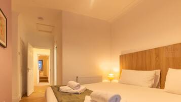 Hotelkamer met een bed, nachtkastje, lamp en uitzicht op een gang.