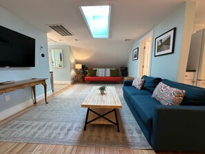 A living room with a large TV, a wooden coffee table, a blue sofa, and a red sofa.