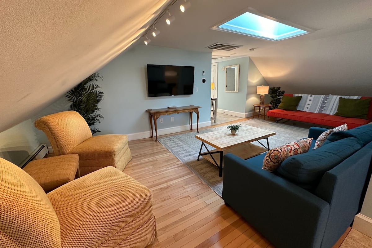 A cozy living room with a sofa, armchair, coffee table, and a flat-screen TV.