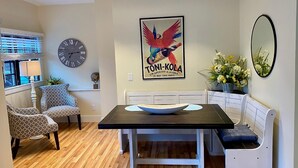 Un comedor con una mesa negra, sillas blancas, un reloj y un cartel enmarcado en la pared.