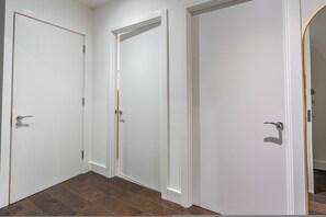 A hallway with three white doors, wooden flooring, and a white wall.