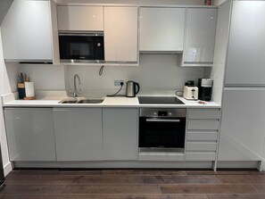 A modern kitchen with grey cabinets, a Bosch microwave, a sink, a kettle, a toaster, and an oven.