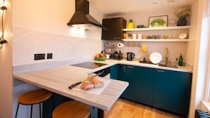 Une cuisine moderne dotée d’un plan de travail en marbre, d’un îlot central avec des tabourets, de meubles de couleur turquoise et d’une hotte noire.