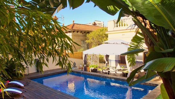 Ein Pool mit Liegestühlen und Sonnenschirmen, umgeben von Grünflächen und Gebäuden.