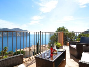Un balcon agrémenté de meubles en osier, d’une table en verre et d’une bouteille de vin rouge.