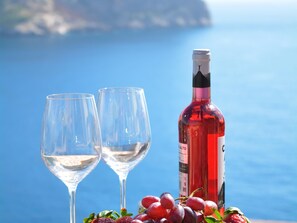 Two empty wine glasses, a bottle of red wine, and a bunch of grapes on a table with a coastal background. - Villa With Incredible sea Views and Pool Sleeps 7 (Andraitx)