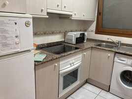 A compact kitchen with a refrigerator, microwave, stove, oven, and washing machine.
