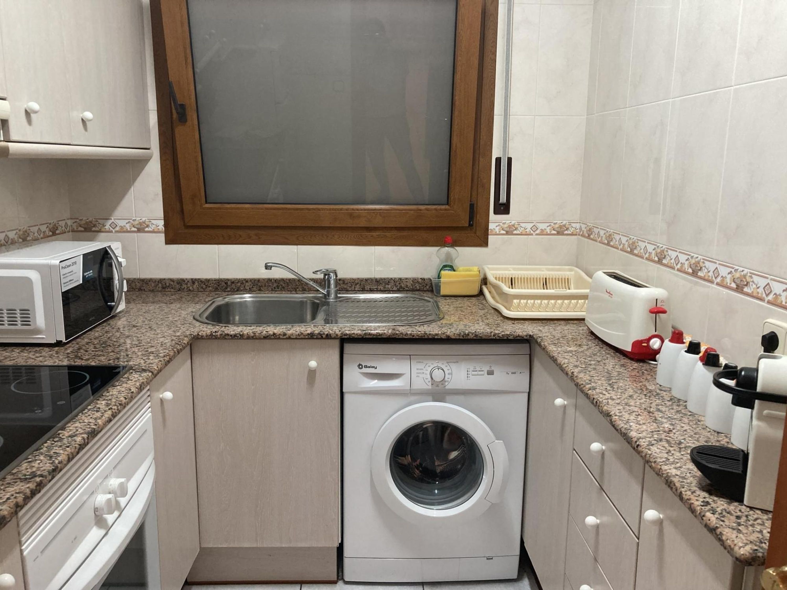 A compact kitchen with a built-in washing machine, a microwave, a toaster, and a sink.