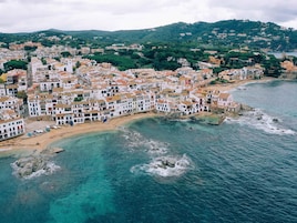 A coastal town with white buildings, a beach, and rocky outcrops in the water.