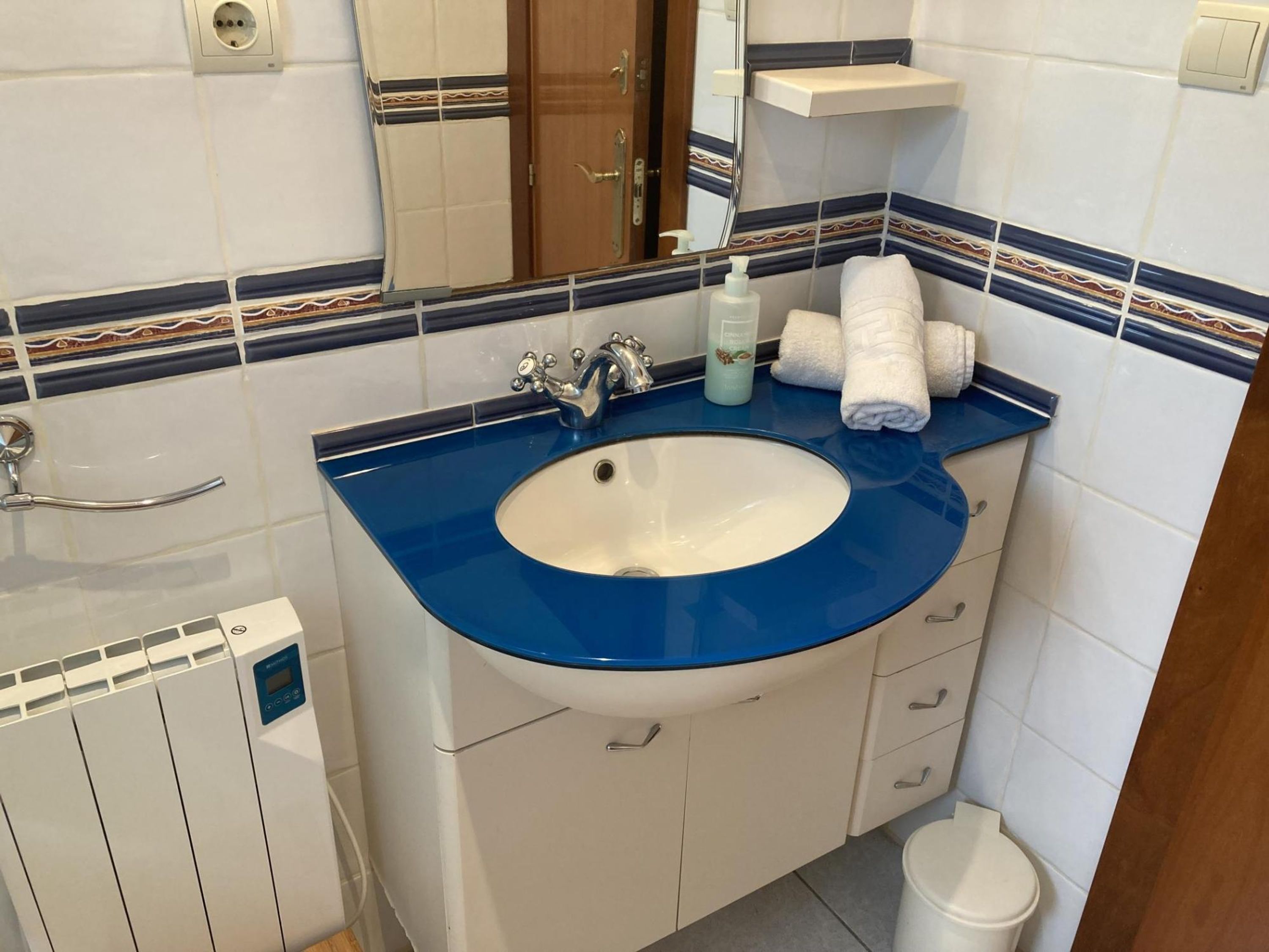 Un bany amb un rentapeus blau, armaris blancs, un mirall i una barra de tovalloles.