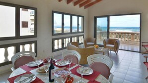 A dining area with a table set for four, large windows, and a view of the ocean. - Mallorca Beach Front Line Apartment 6 Pers (Santa Margalida)