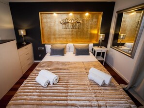 Ein Hotelzimmer mit einem großen Bett, zwei Nachttischen inklusive Lampen, einer Kopfteil mit goldenem Dekor und einem großen Spiegel an der Wand.