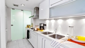 Una cocina moderna con armarios blancos, fregaderos de acero inoxidable y una puerta de vidrio que da a otra habitación.