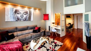 A modern living room with a grey sofa, a red accent wall, and a Buddha painting. - Victoria City Center 1 Downtown Luxury Duplex (Barcelona)