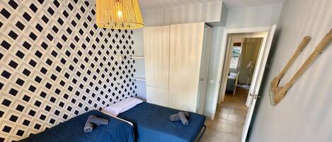 A bedroom with two beds, a patterned wall, a hanging light fixture, and a wooden spoon on the wall.