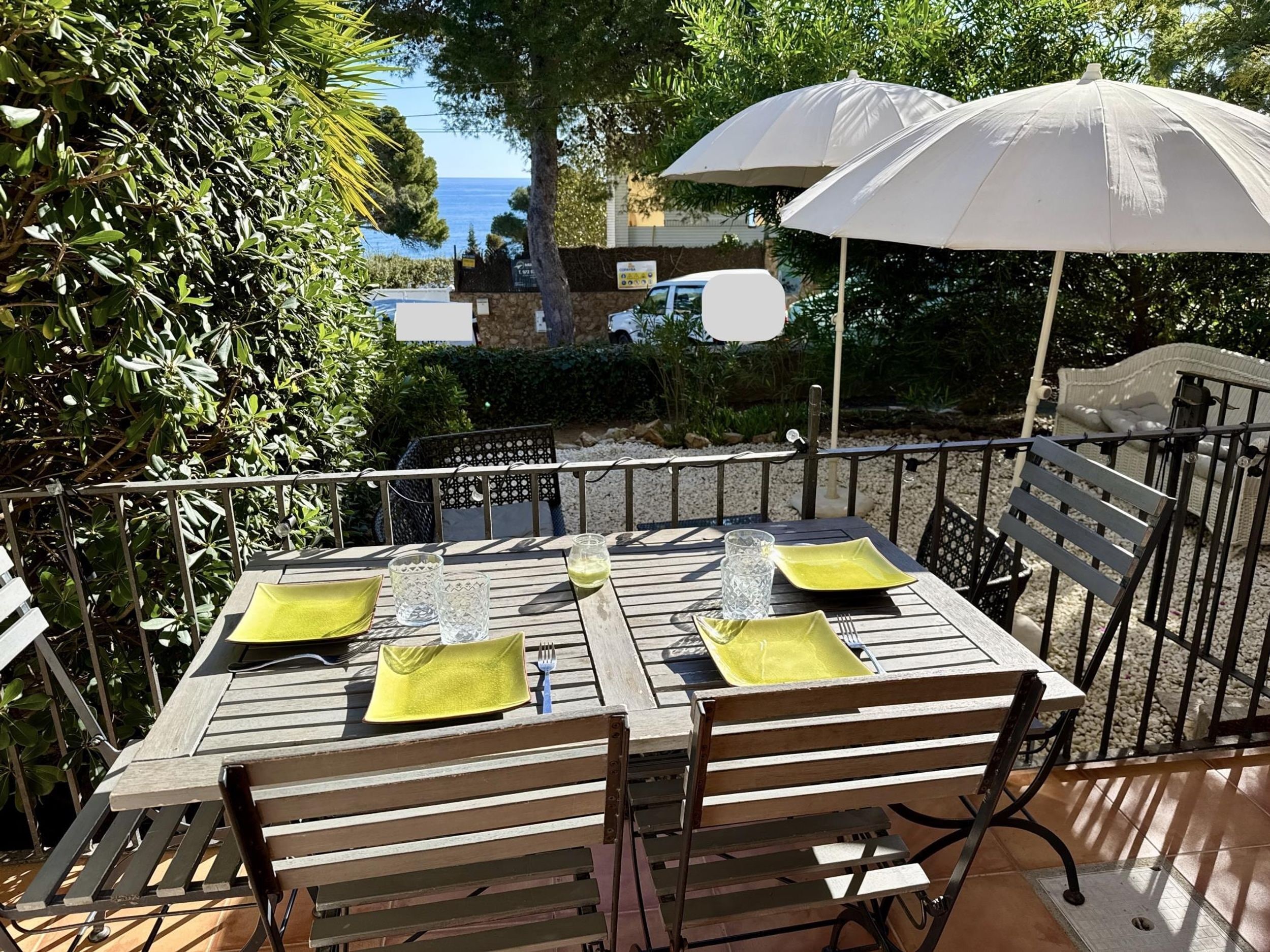An outdoor dining area with a table set for two, two umbrellas, and a view of the sea.