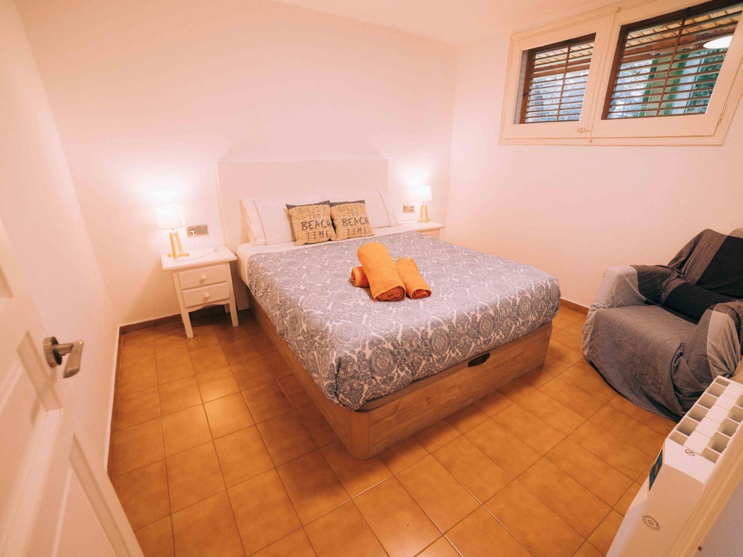 A bedroom with a bed, nightstands, a chair, and a window with blinds.
