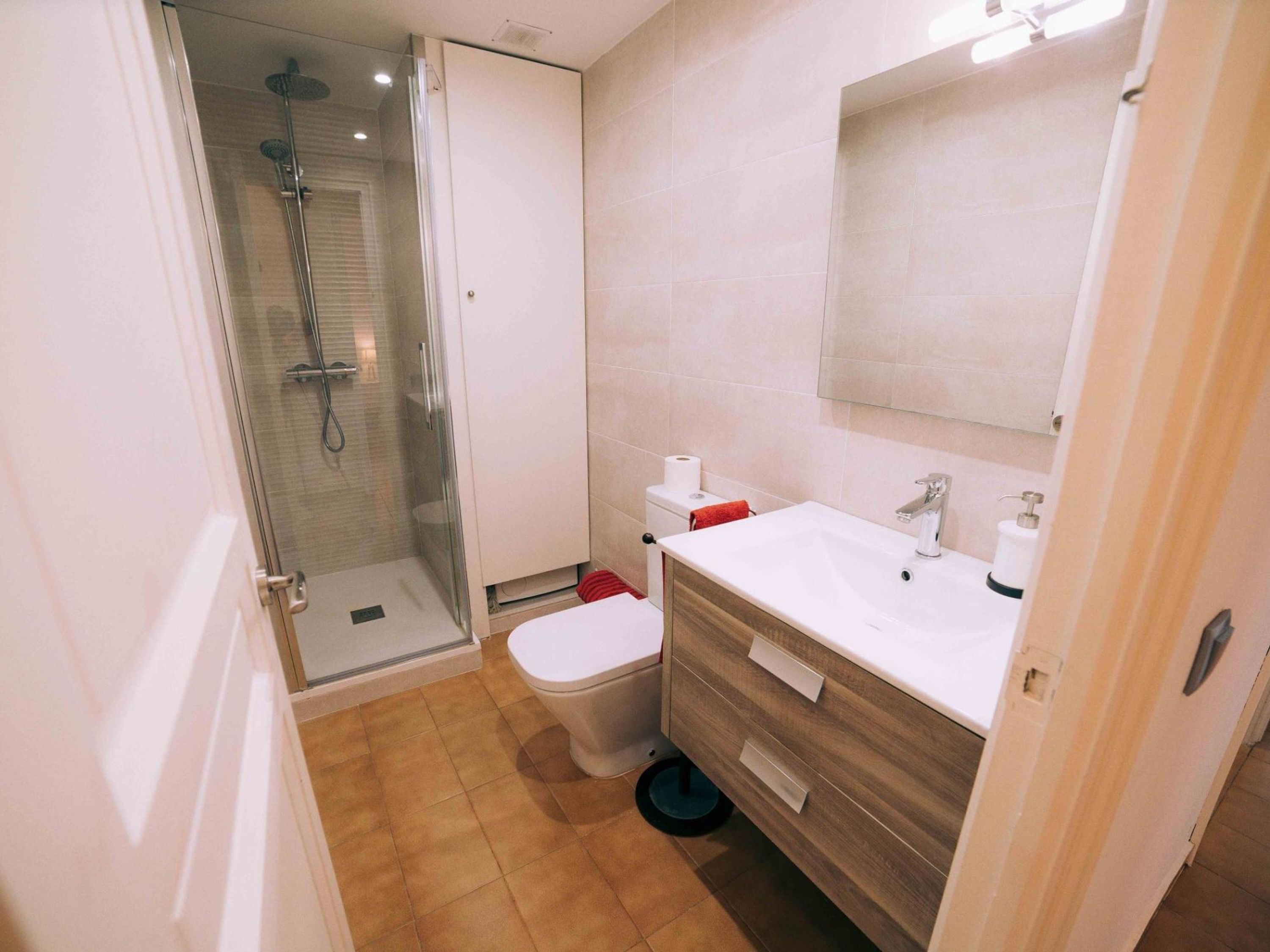 Une salle de bain moderne avec une douche à parois de verre, des toilettes blanches, un meuble-lavabo en bois avec un miroir et un évier.