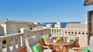 A balcony with a round wooden table set for breakfast, overlooking a coastal view.