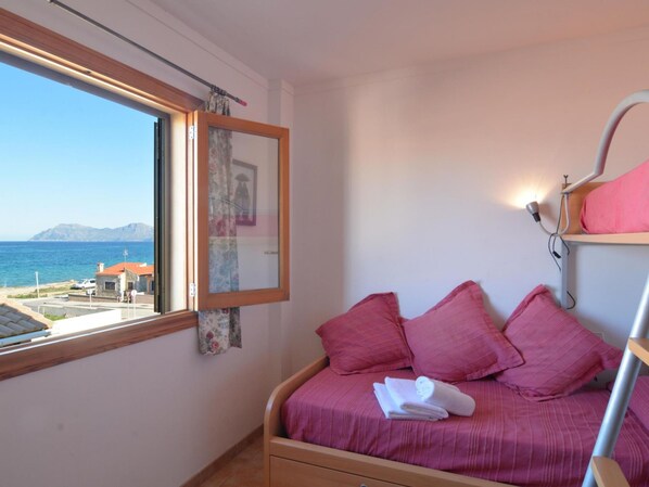 A bedroom with a bed, pink pillows, a window with a view of the sea, and a wooden ceiling.