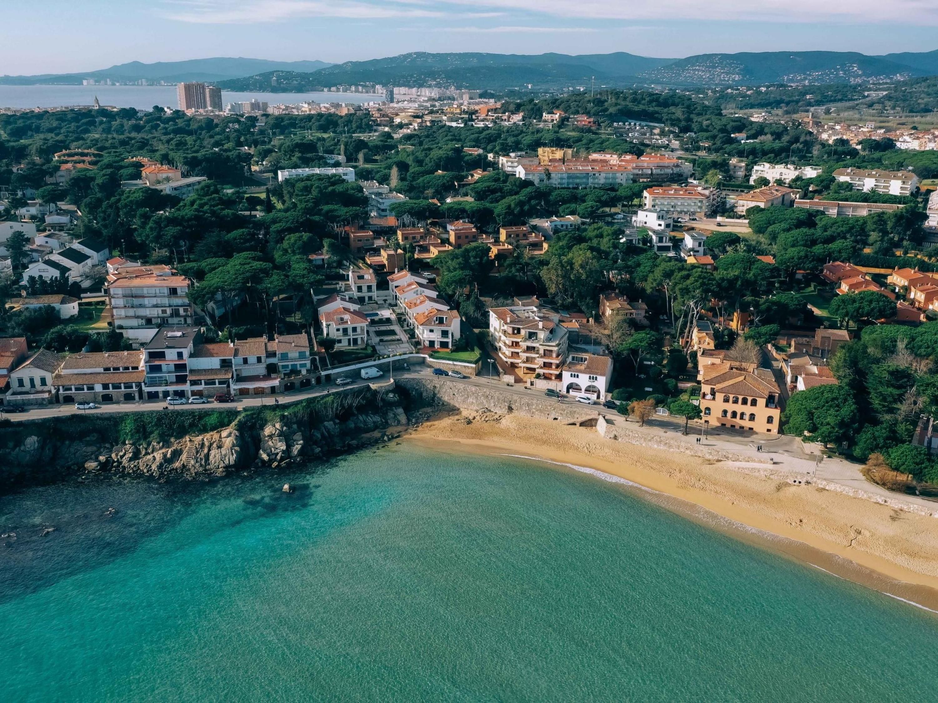 An aerial view of a coastal town with residential buildings, a beach, and a clear view of the sea.