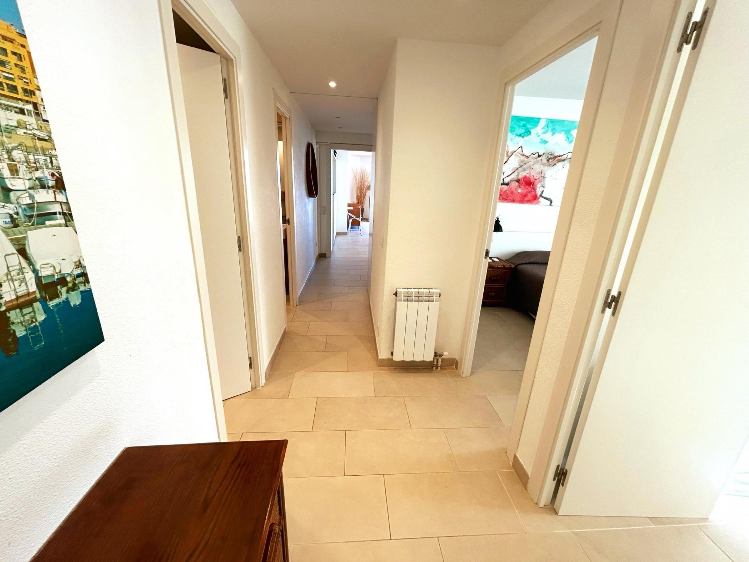 Een gang met een houten bank, een radiator en een deur die uitkomt in een ruimte met uitzicht op boten.