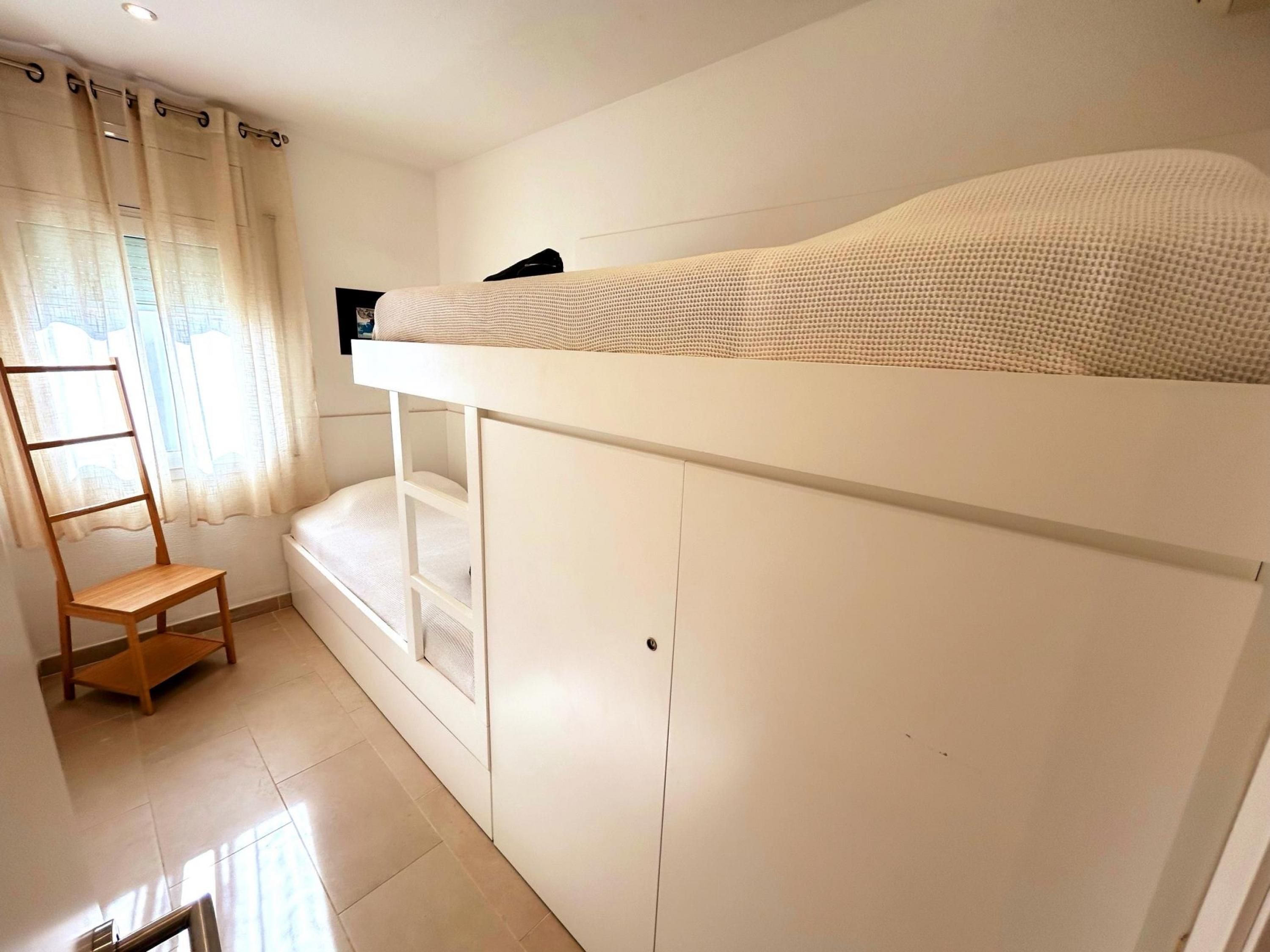 A bunk bed room with a ladder, a chair, and a window with curtains.
