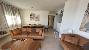 A modern living room with a brown leather sofa, a wooden coffee table, and a dining area with a large table and chairs. - Charming Apartment in La Fosca Beach (Palamós)