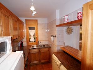 Una cocina compacta con armarios de madera, horno integrado, lavamanos y un reloj en la pared.
