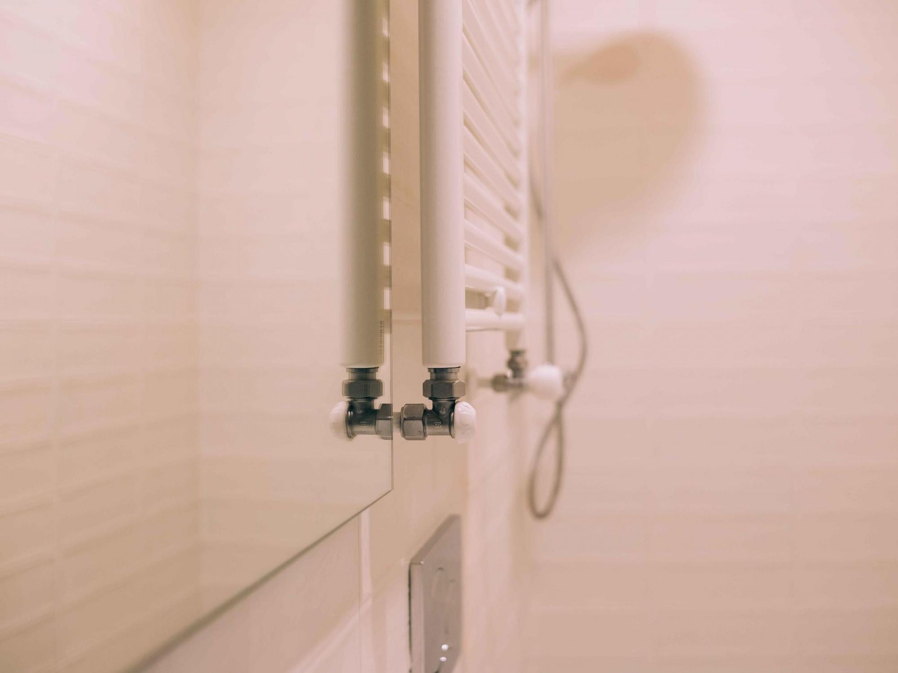 Un baño con pared de azulejos blancos, radiador blanco y tubería visible.