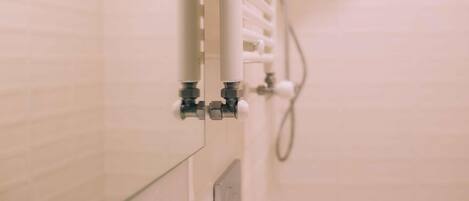 Un baño con pared de azulejos blancos, radiador blanco y tubería visible.