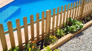 A rectangular swimming pool with a wooden fence and a garden bed with various plants and flowers. - Casa Rural en el Centro Hist Rico de Gualta (Gualta)